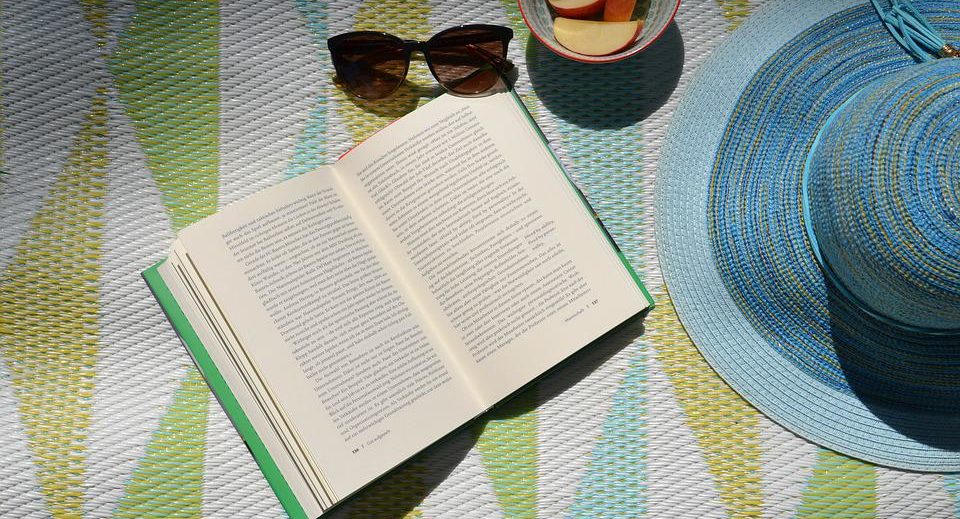 Photo: Un livre ouvert posé sur une couverture avec un chapeau et des lunettes de soleil